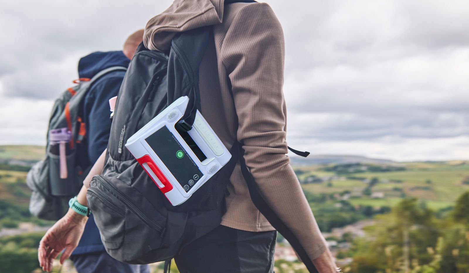 Elliot AED clipped to a hiking backpack on a trail